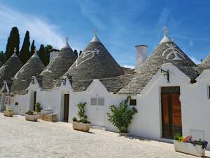 Trulli in Alberobello mit kugelförmigen Dachspitzen und schützenden Zeichen auf dem natursteinfarbenen Dach.
