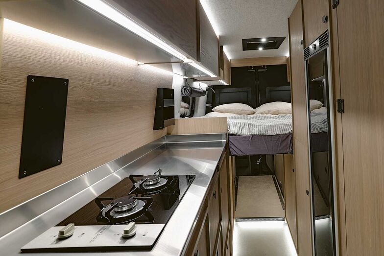 La cuisine présente un robuste plan de travail en inox, un évier, une plaque de cuisson à deux feux et un grand réfrigérateur.