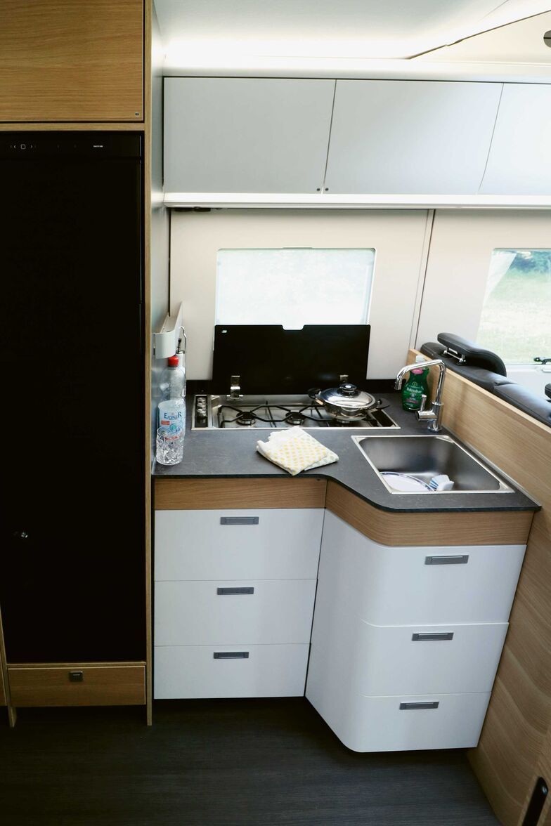 La cuisine avec placard inférieur en L offre beaucoup d’espace de rangement, un plan de travail suffisant et un grand évier avec solide mitigeur monocommande.