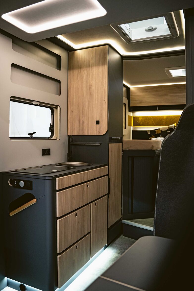 L’armoire haute comporte en bas un réfrigérateur et en haut un espace de rangement auquel il est possible d’accéder aussi bien depuis la cuisine que depuis le lit.